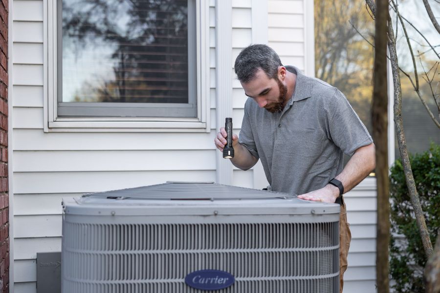 Technician inspecting a residential condenser unit beside a home